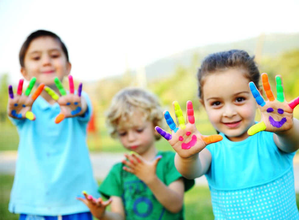 3Kinder mit bunten Händen auf Wiese